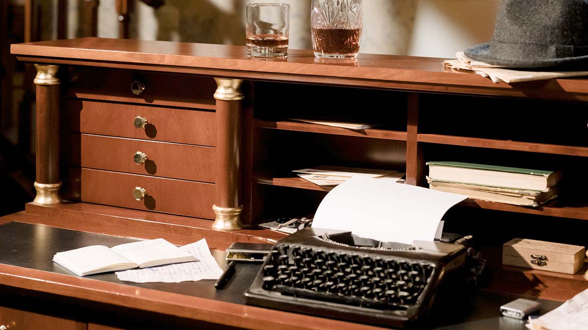 advice for writers: an old fashioned desk with a typewriter and glass of whiskey